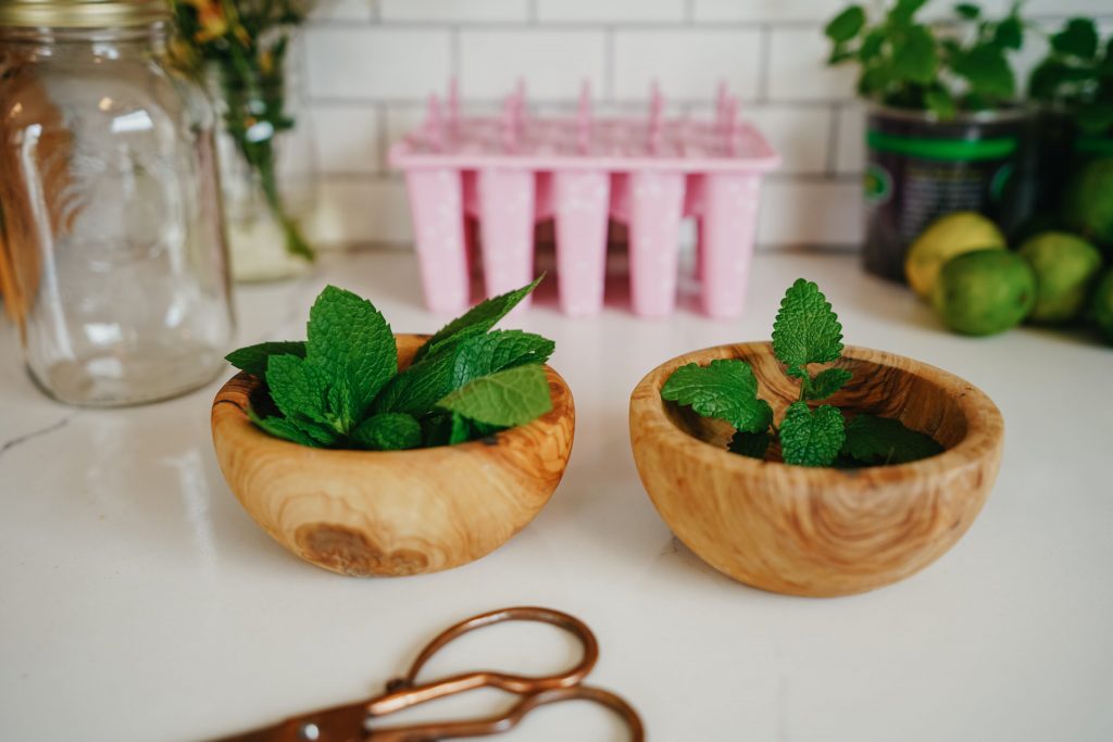 Fresh healing herbs on a wooden board beside a mug ready to make herbal tea.